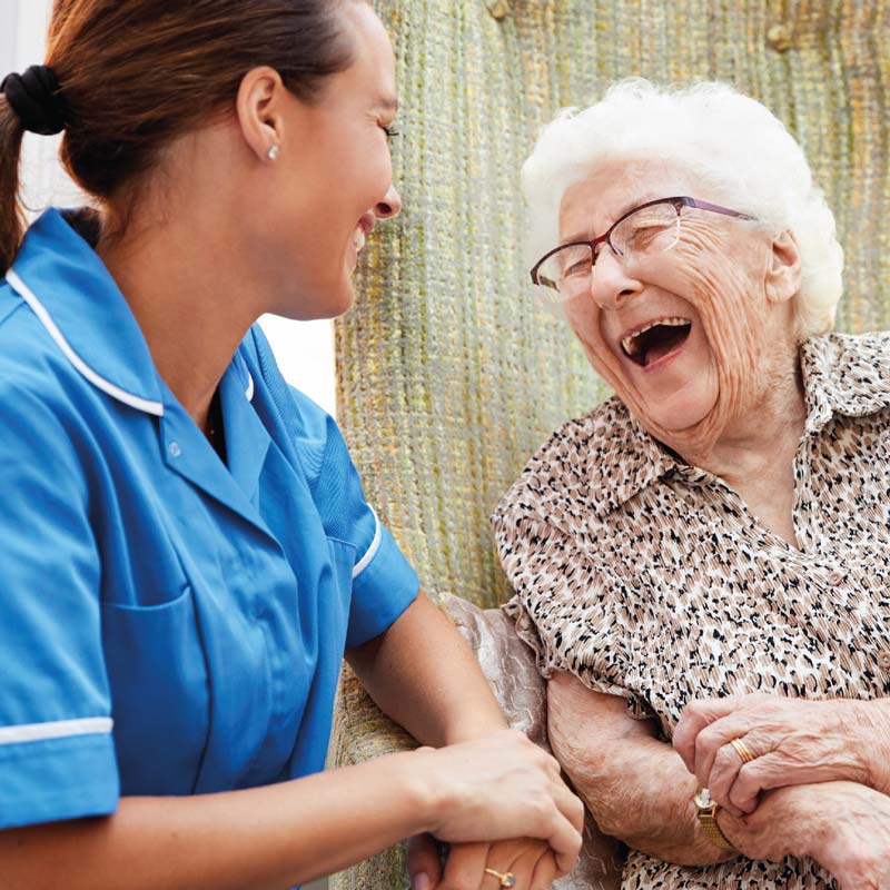 Elderly lady laughing with carer sat by her side