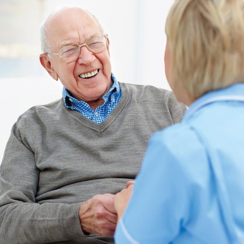 Elderly man laughing with carer who is blurred in foreground