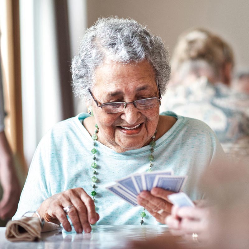 Elderly lady smiling, looking down at her hand of cards