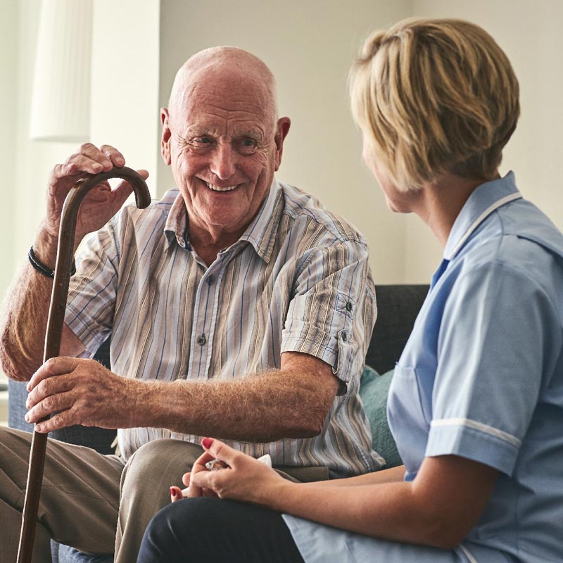 Man sat with walking stick next to carer on sofa