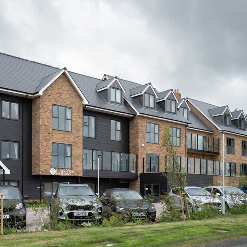 Large sand brick and grey modern building complex with car parking and lawn in foreground